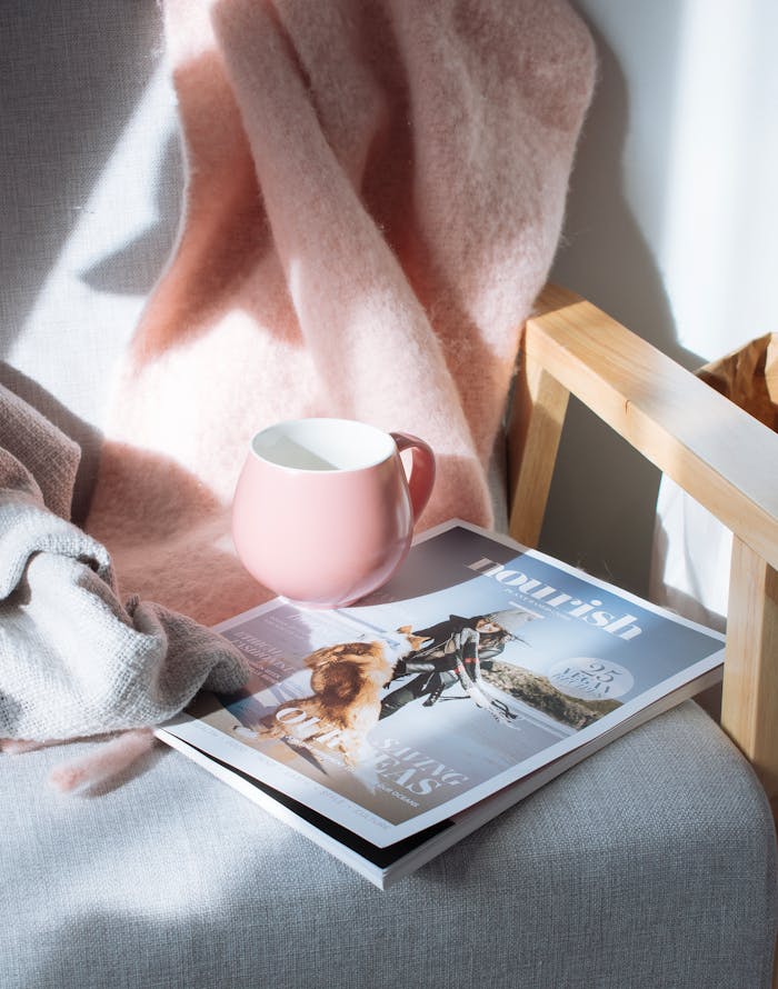 A warm scene featuring a pink mug and magazine on a wooden chair, bathed in sunlight.