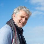 Portrait of a smiling senior man wearing a scarf against a blue sky, conveying warmth and cheerfulness.